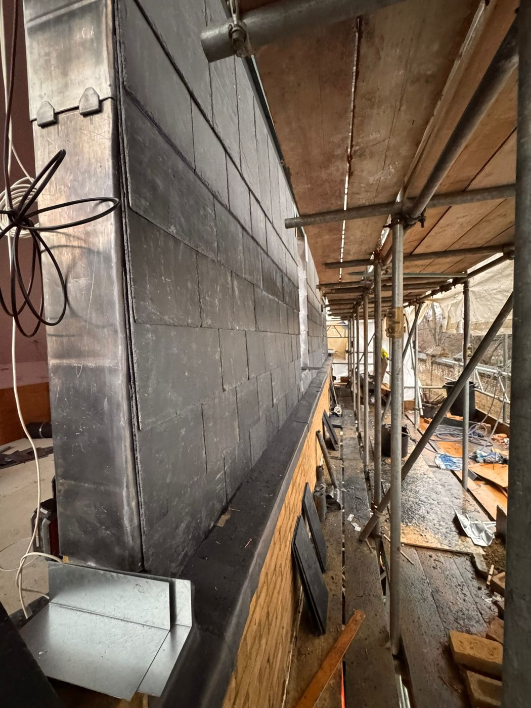 Close side view of slate-style roofing beneath scaffolding
